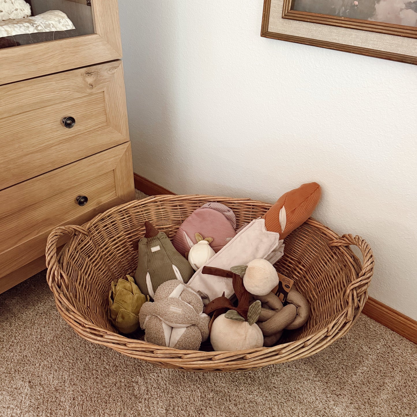 Wicker basket filled with soft toys on a carpeted floor next to wooden furniture.