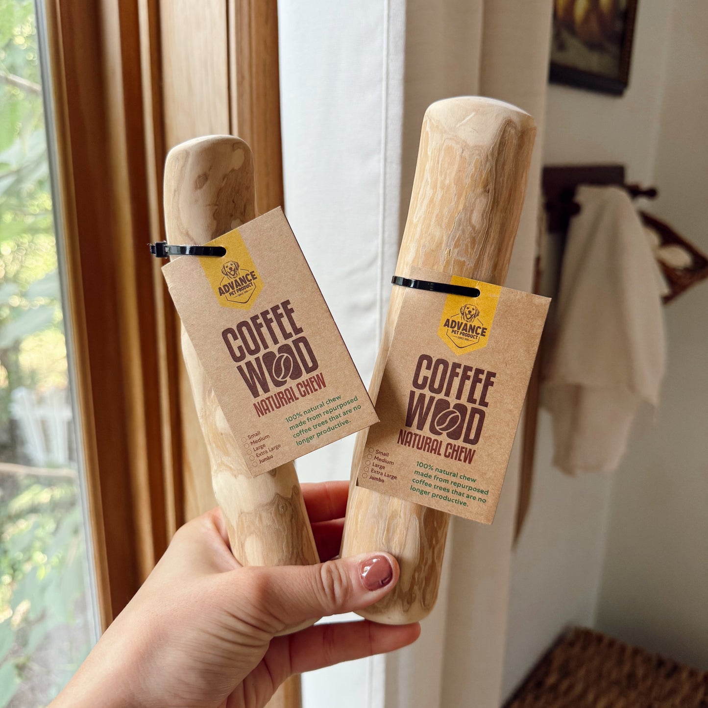 Two 'Coffee Wood' natural chew products held by a hand in front of a window.