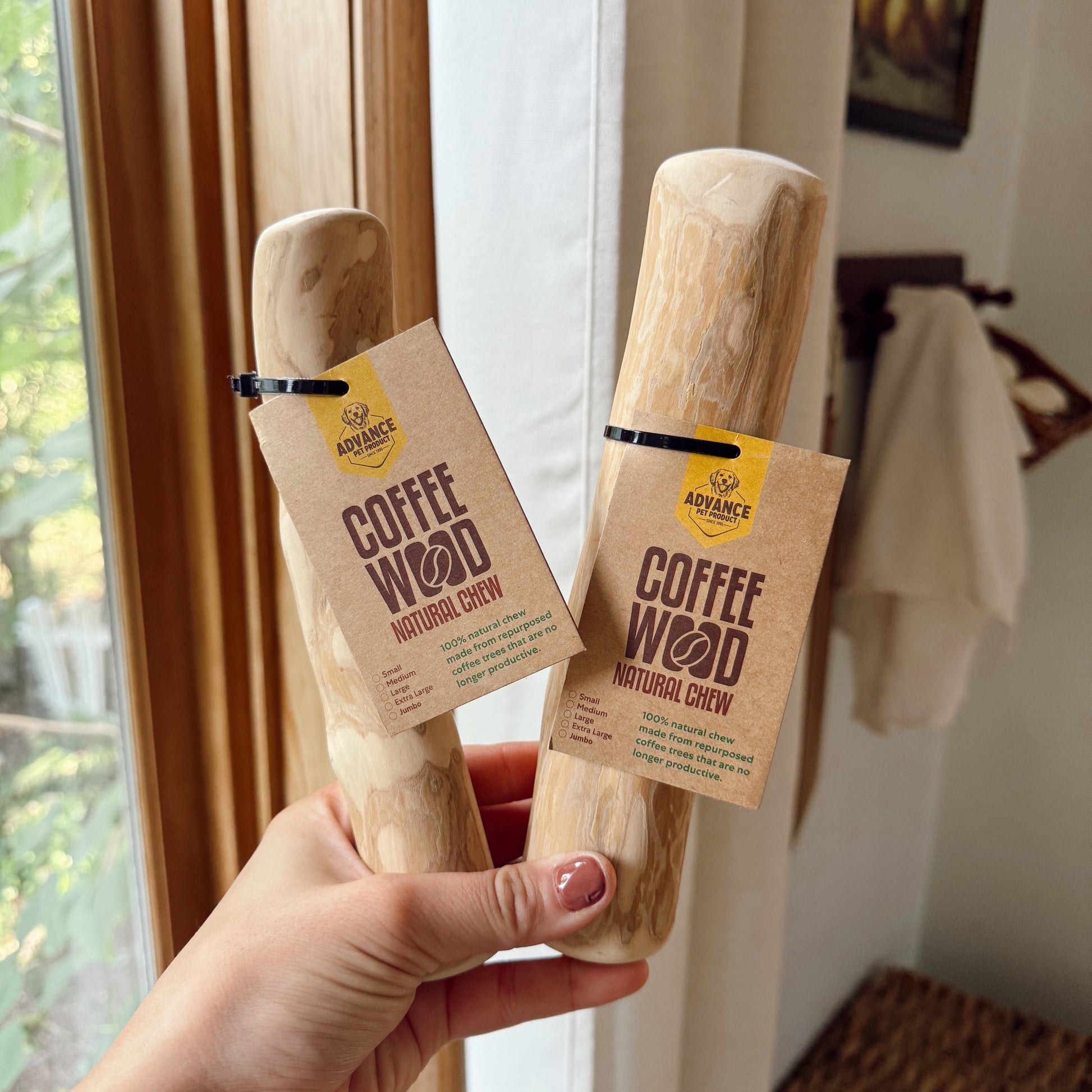 Two 'Coffee Wood' natural chew products held by a hand in front of a window.