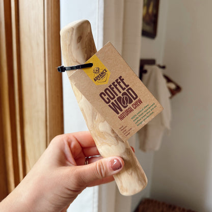 Hand holding a dog coffee wood stick indoors.