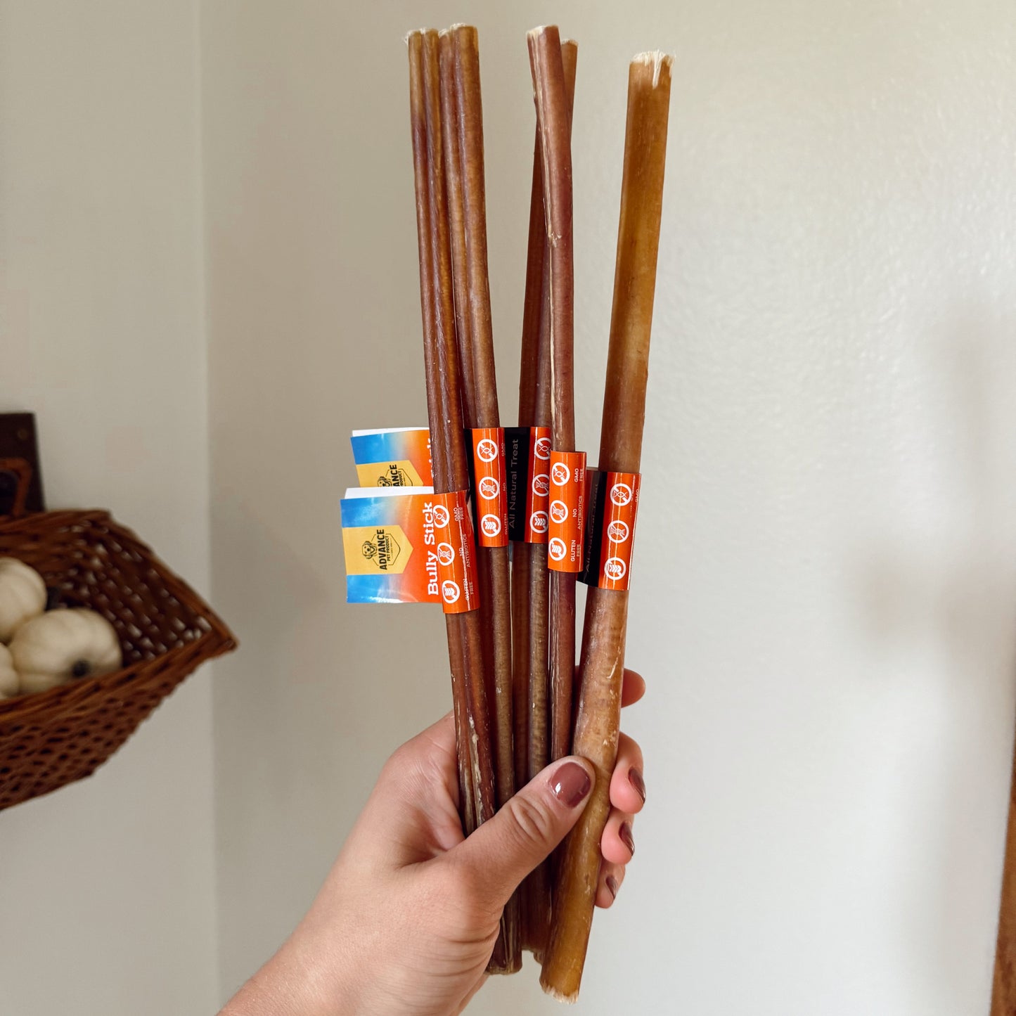 Hand holding a bundle of dog bully sticks with packaging in the background.