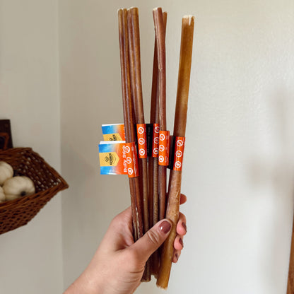 Hand holding a bundle of dog bully sticks with packaging in the background.