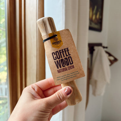 Hand holding a dog coffee wood stick indoors.