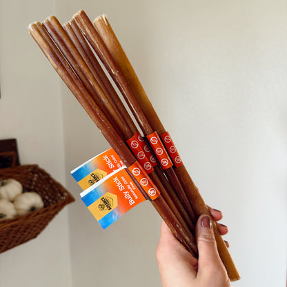 Hand holding a bundle of dog bully sticks with packaging in the background.