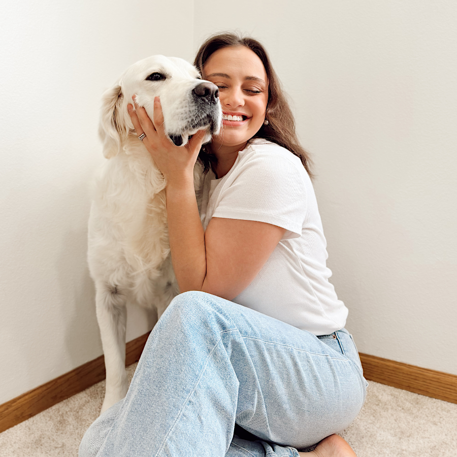 Woman sitting on the floor with a white dog, both looking happy.
