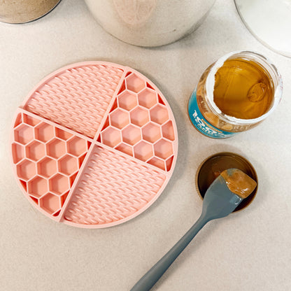 Pink dog lick mat on a kitchen counter with peanut butter and a spatula.