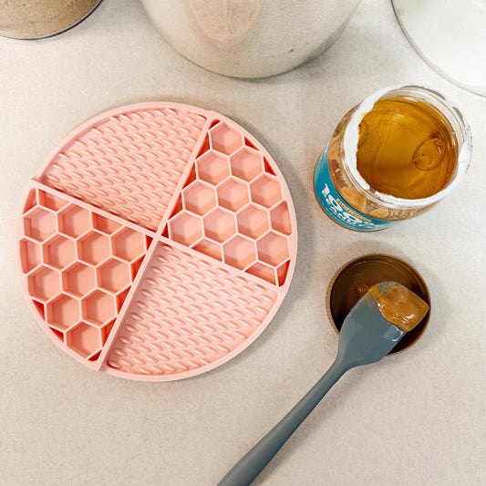Pink dog lick mat on a kitchen counter with peanut butter and a spatula.