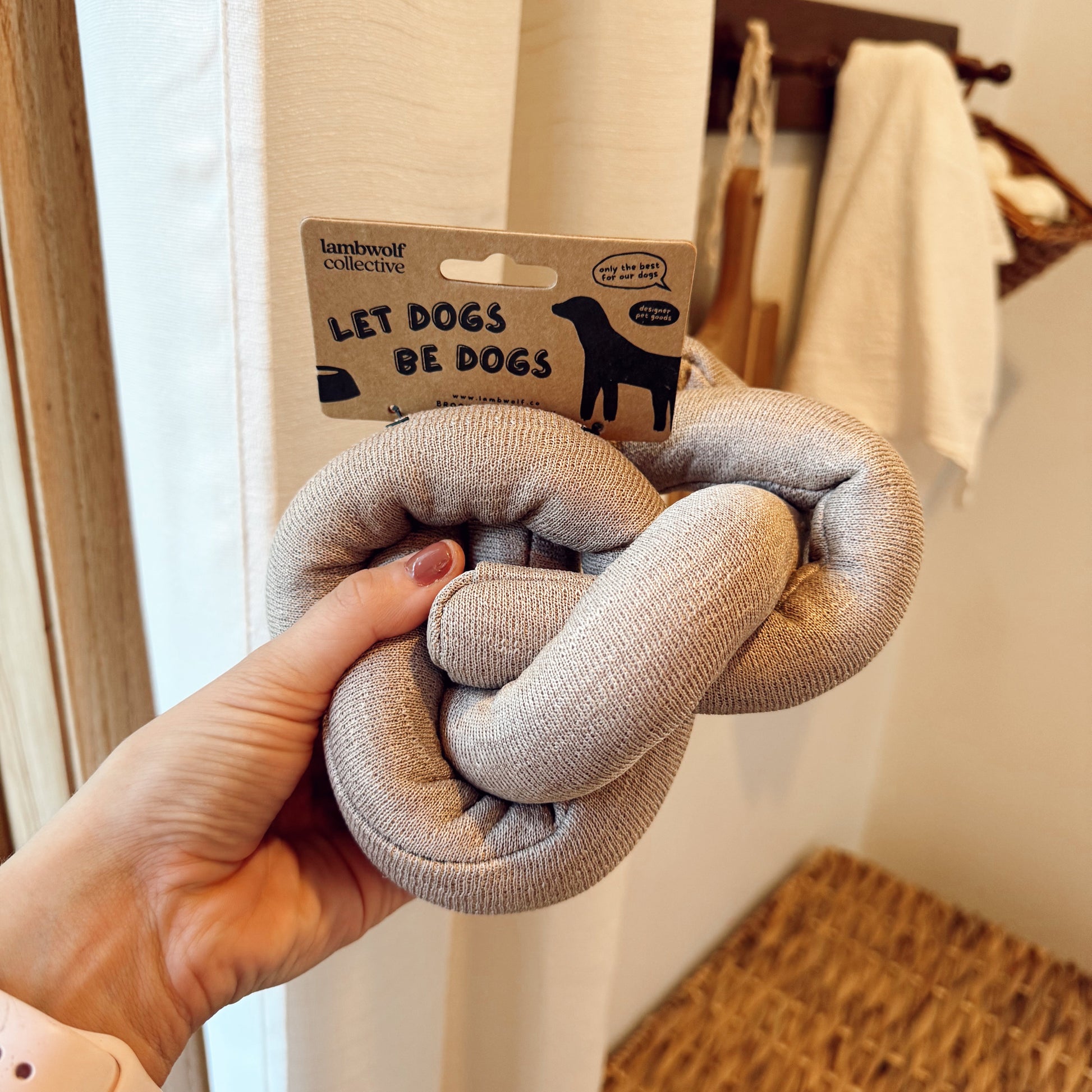 Hand holding a knot dog toy indoors.