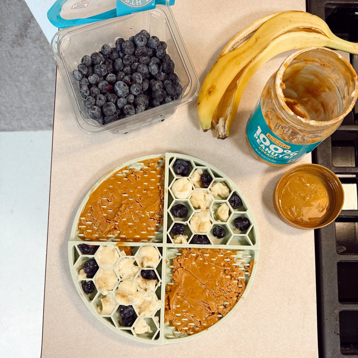 Kitchen counter with a round lick mat filled with peanut butter, bananas, and blueberries.