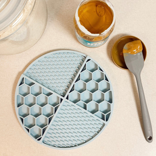 Silicone dog lick mat with honeycomb pattern on a beige surface with a jar of peanut butter and spoon.