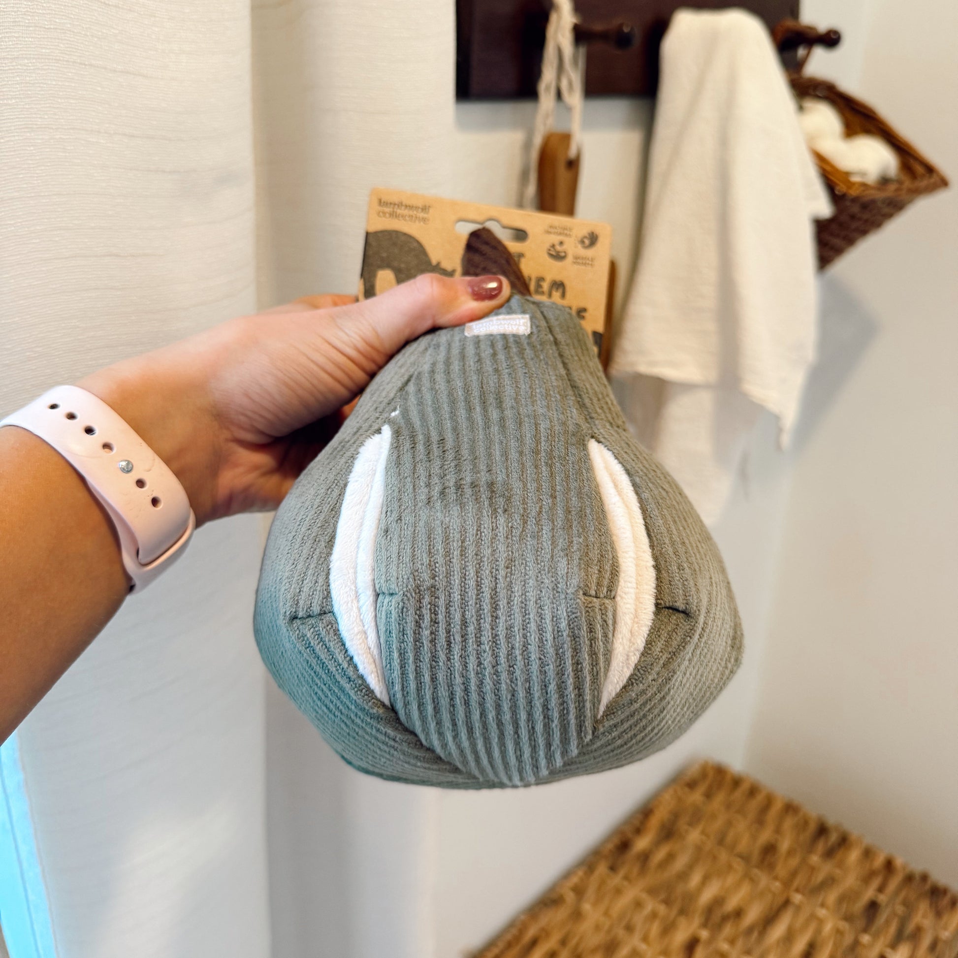 Hand holding a butternut dog toy indoors.