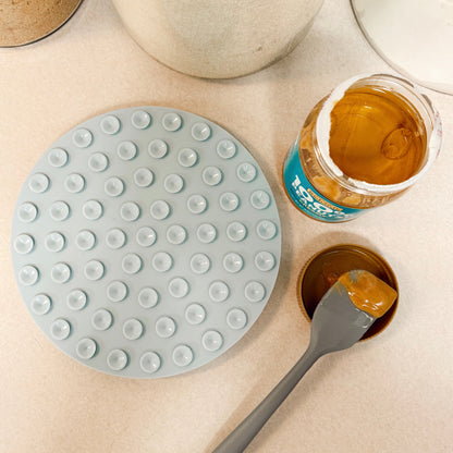 Light blue silicone dog lick mat upside down with jar of peanut butter and spatula on a white countertop.