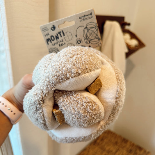 Hand holding a textured knot ball dog toy with treats in it indoors.