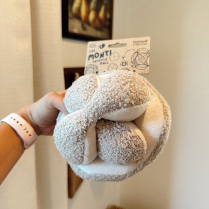 Hand holding a textured ball dog toy indoors.