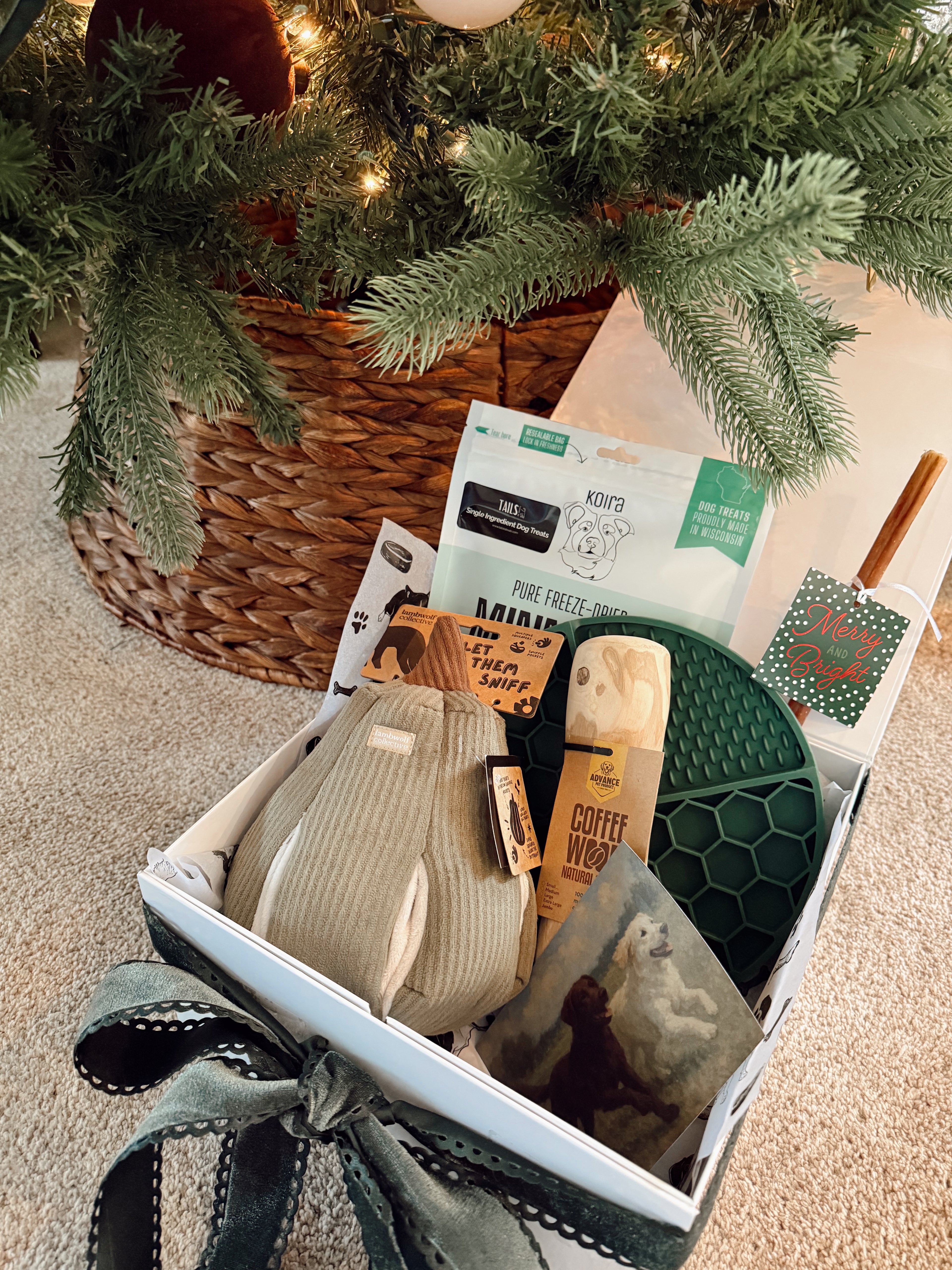 Gift basket with pet products under a decorated Christmas tree.